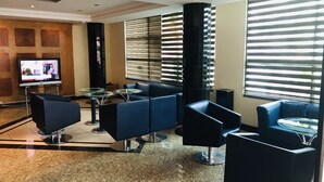 A modern lounge area with a flat-screen TV, comfortable seating, and large windows with blinds. - Golden Park Hotel (Luanda)