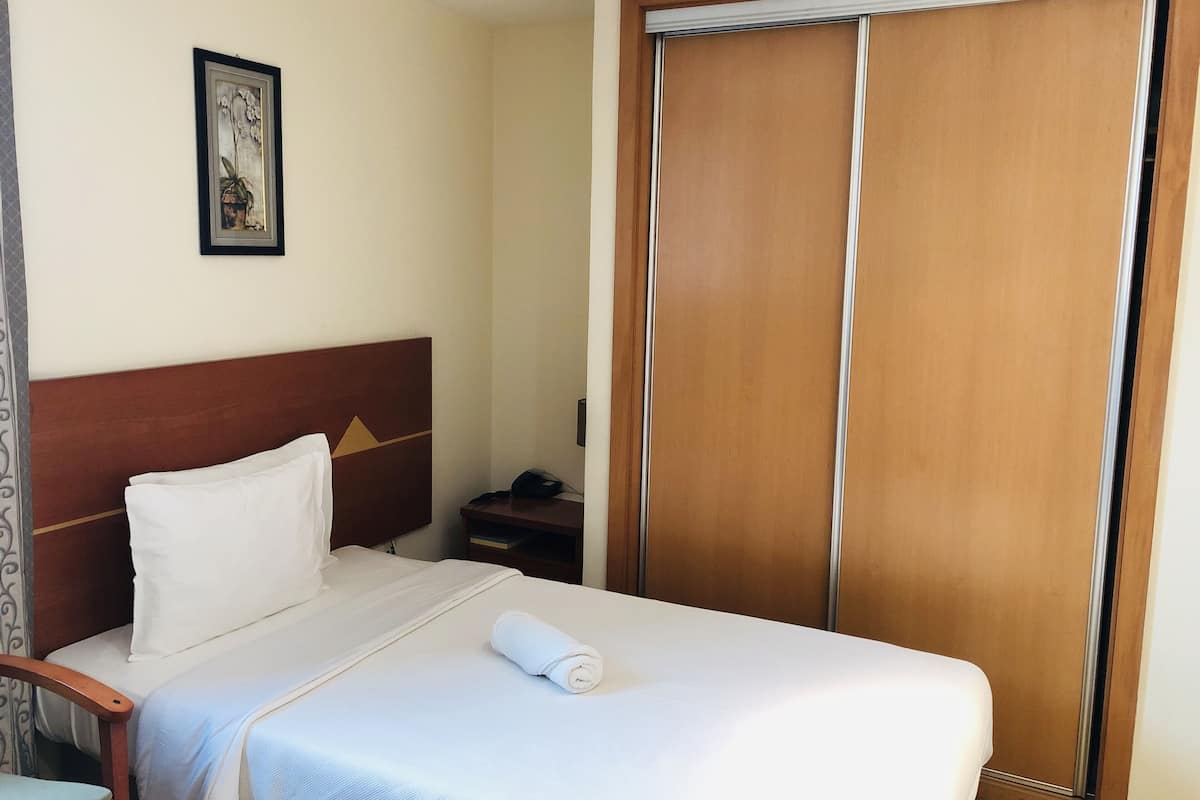 Habitación de hotel con cama, cabecera de madera, mesita de noche, teléfono y armario.