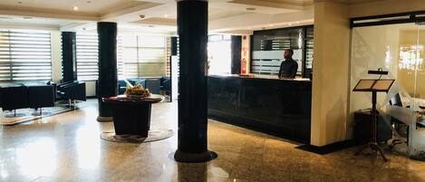 A spacious lobby with a reception desk, seating area, and a piano.