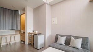 A compact living space with a grey sofa, a small table, a kitchenette, and a wooden cabinet. - CJ Hotel (Taipei)