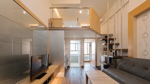 A modern living room with a flat-screen TV, wooden flooring, a grey sofa, and a wooden coffee table. - CJ Hotel (Taipei)