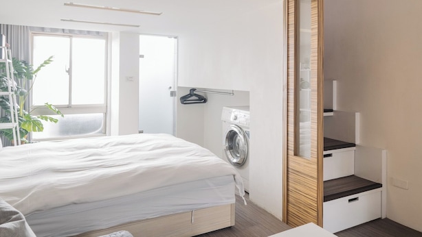 A modern bedroom with a bed, a washing machine, a small table, and a mirror. - CJ Hotel (Taipei)