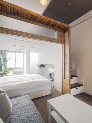 A modern bedroom with a bed, a washing machine, a small table, and a mirror.