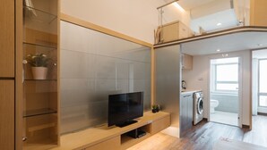 A modern kitchen with a built-in washing machine, a flat-screen TV, and a glass-fronted cabinet with a potted plant. - CJ Hotel (Taipei)