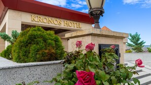 The exterior of the Kronos Hotel with a clear entrance, a well-maintained hedge, and a lamp post.