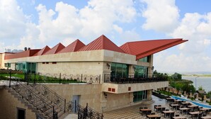 A modern building with a unique architectural design, featuring a pool and outdoor seating area with a view of a large body of water.