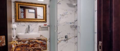 Une salle de bain avec un lavabo en marbre, une douche en verre et un miroir avec un cadre doré.