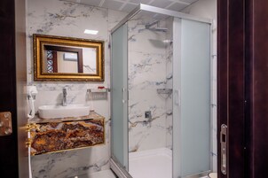 Un baño con lavamanos de mármol, ducha con cerramiento de vidrio y espejo con marco dorado.