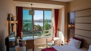 A hotel room with a large window, a bed, a desk, and a chair.