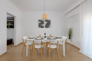 A dining area with a white table set for four, surrounded by white chairs. There are two framed abstract artworks on the wall above the table. -  Harmony Elegant Central Apartment (Rhodes)