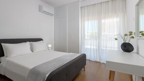 A modern bedroom with a bed, bedside table, and a window with sheer curtains.