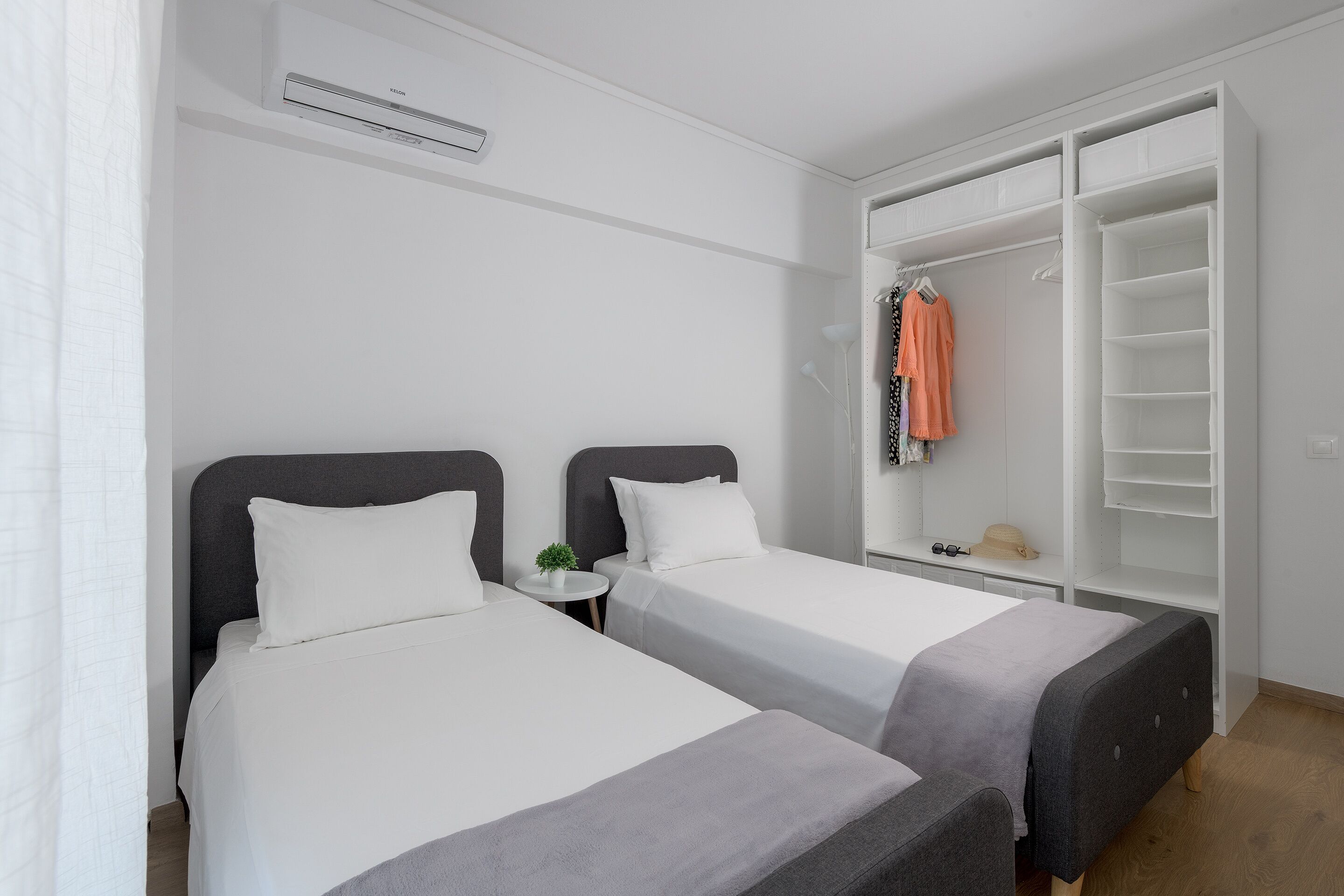 A hotel room with two beds, a wardrobe, and a small table with a plant.