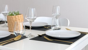 A dining table set with plates, glasses, cutlery, and a woven basket with greenery.