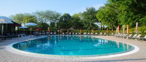Una piscina con sillas de descanso y sombrillas, rodeada de árboles.