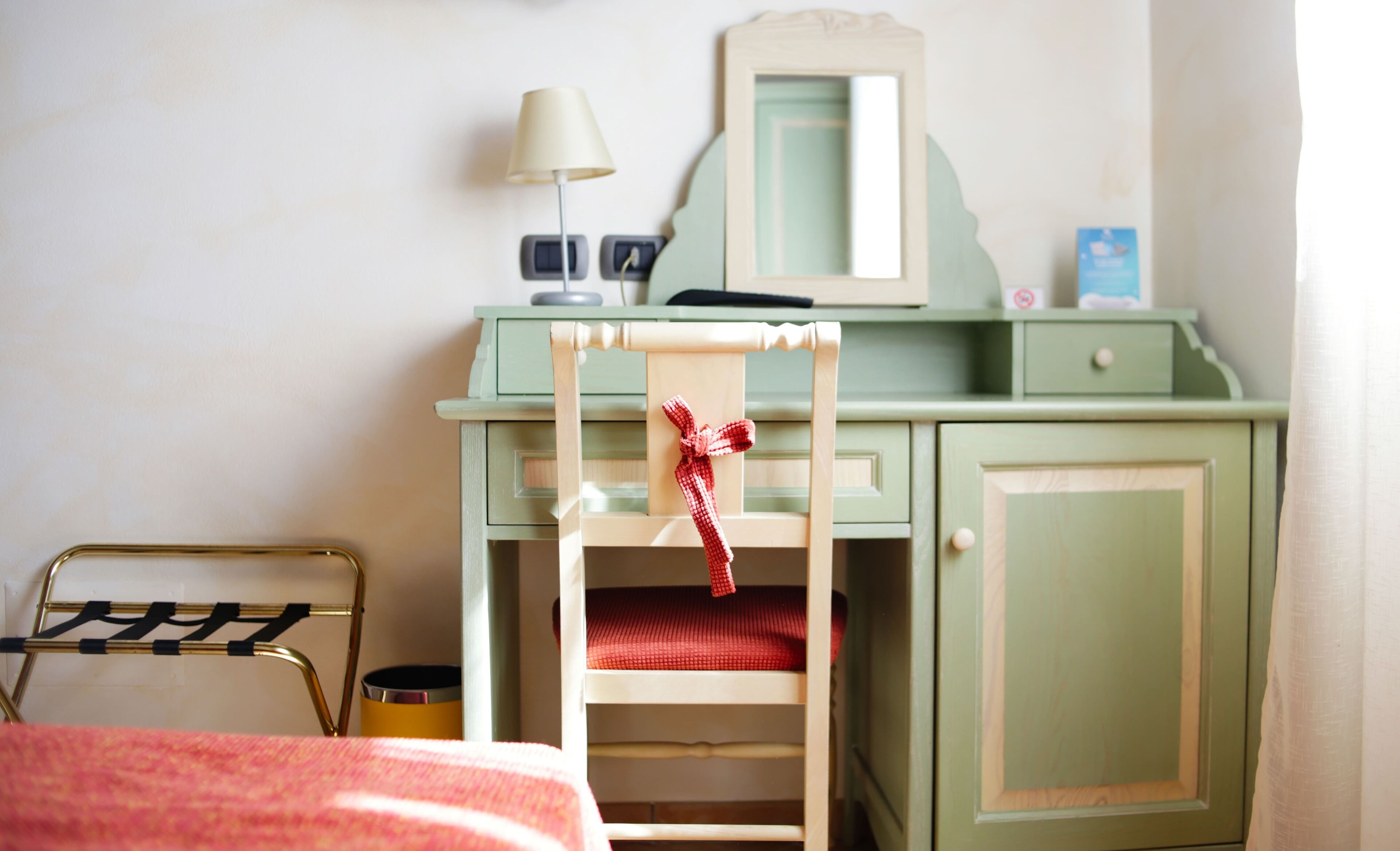 A bedroom with a bed, a chair, a desk, a mirror, and a lamp.