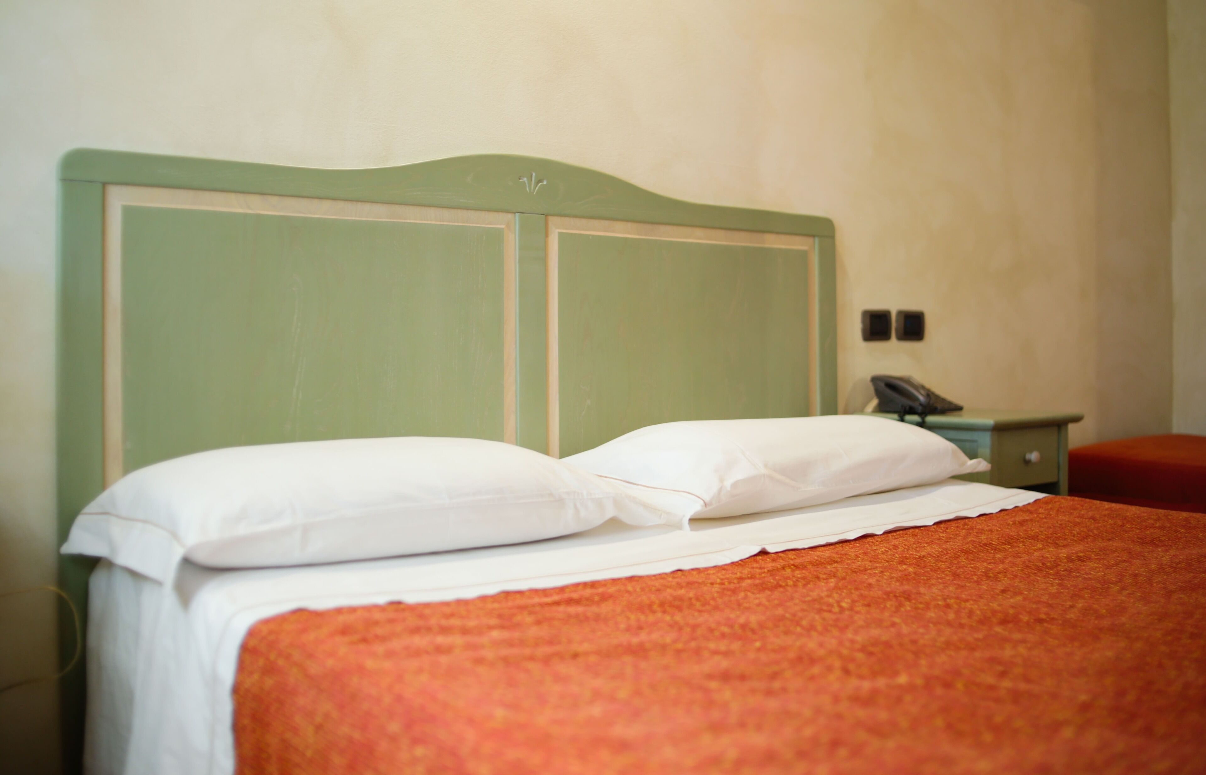A bed with a green headboard, white pillows, and an orange blanket.