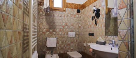 Un baño con piso de baldosas, lavamanos, bidé y ventana.