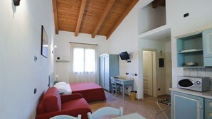 Una habitación pequeña con techo de madera, una mesa de comedor, dos camas rojas, un escritorio, un televisor y una kitchenette.