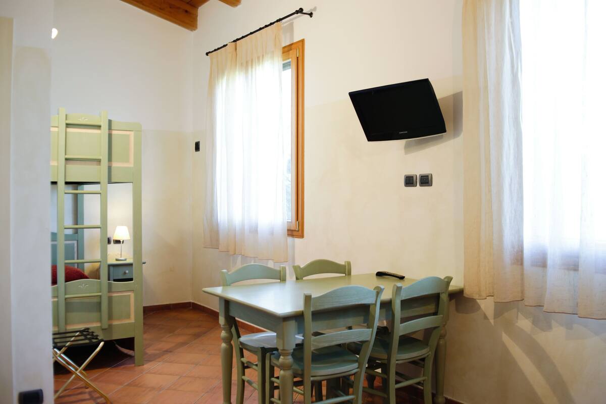 A room with a dining table, chairs, a TV mounted on the wall, and a window with curtains.