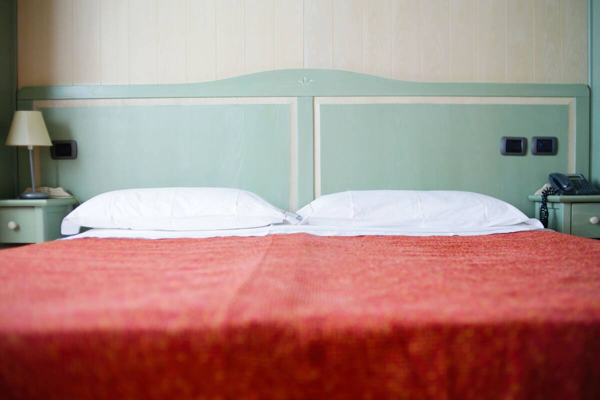 A bed with white pillows and a red bedspread in a room with green walls and a wooden headboard.