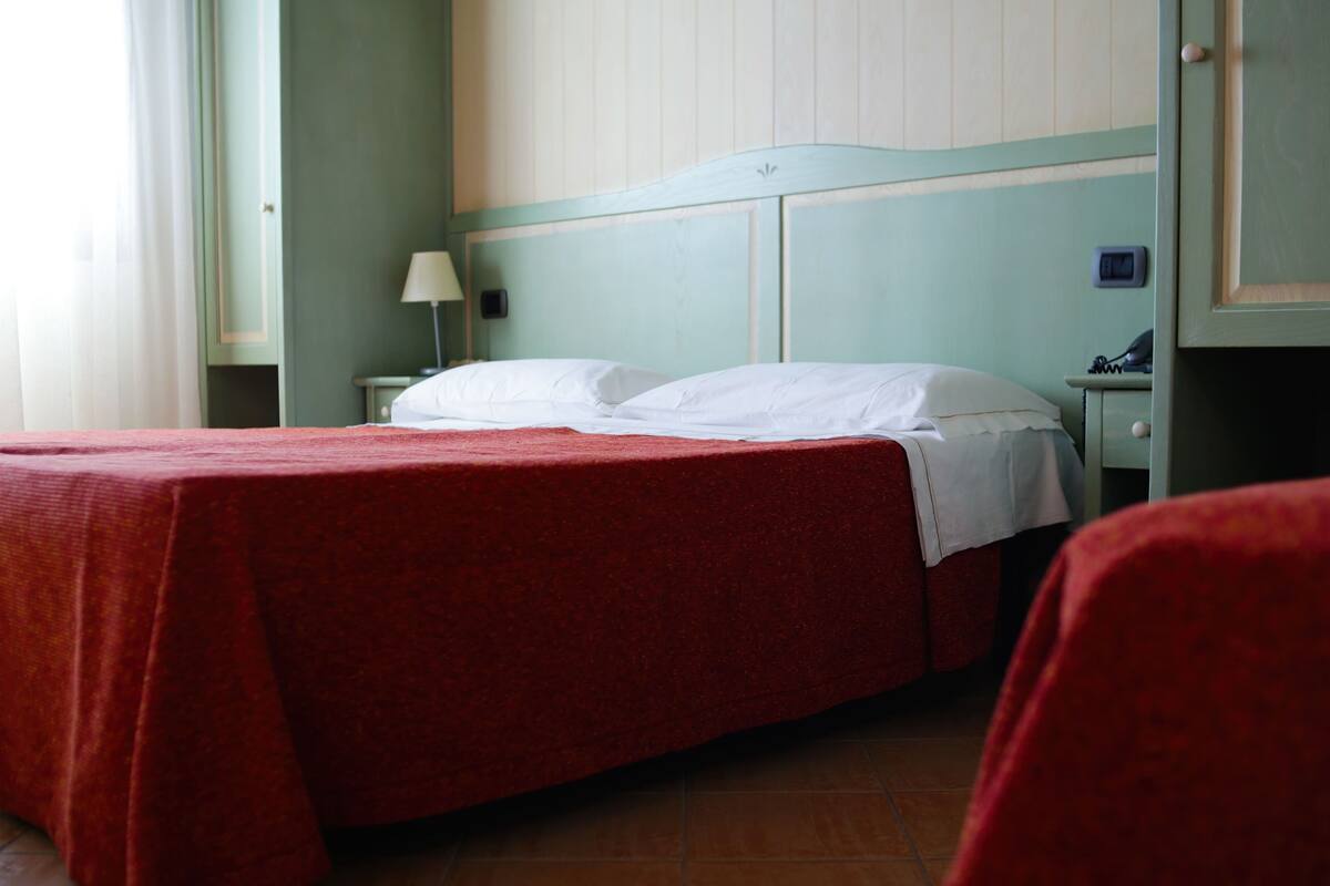 A hotel room with a single bed, a nightstand, a lamp, and a small table with a telephone.