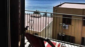 Ein Balkon mit Meerblick, ein Gebäude im Hintergrund und eine Metallreling.