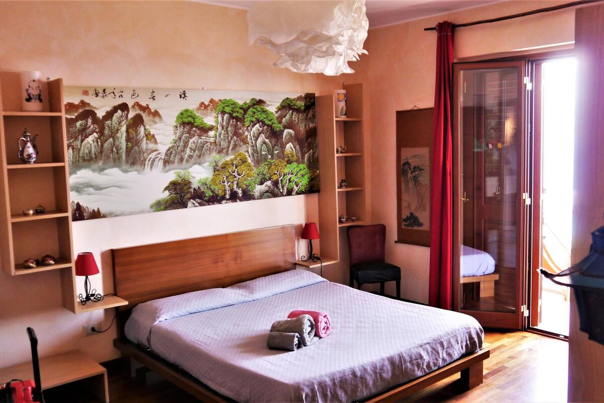 Un dormitorio con una cama grande, un cabecero de madera, una silla roja, un armario de madera y un cuadro en la pared.
