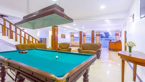 Een pooltafel in een goed verlichte kamer met een trap, comfortabele zitplaatsen en uitzicht door grote ramen.