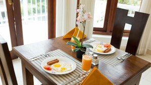 A wooden dining table with a plate of eggs, a glass of orange juice, and a small plant. - Orchid Villa Kandy (Kandy)