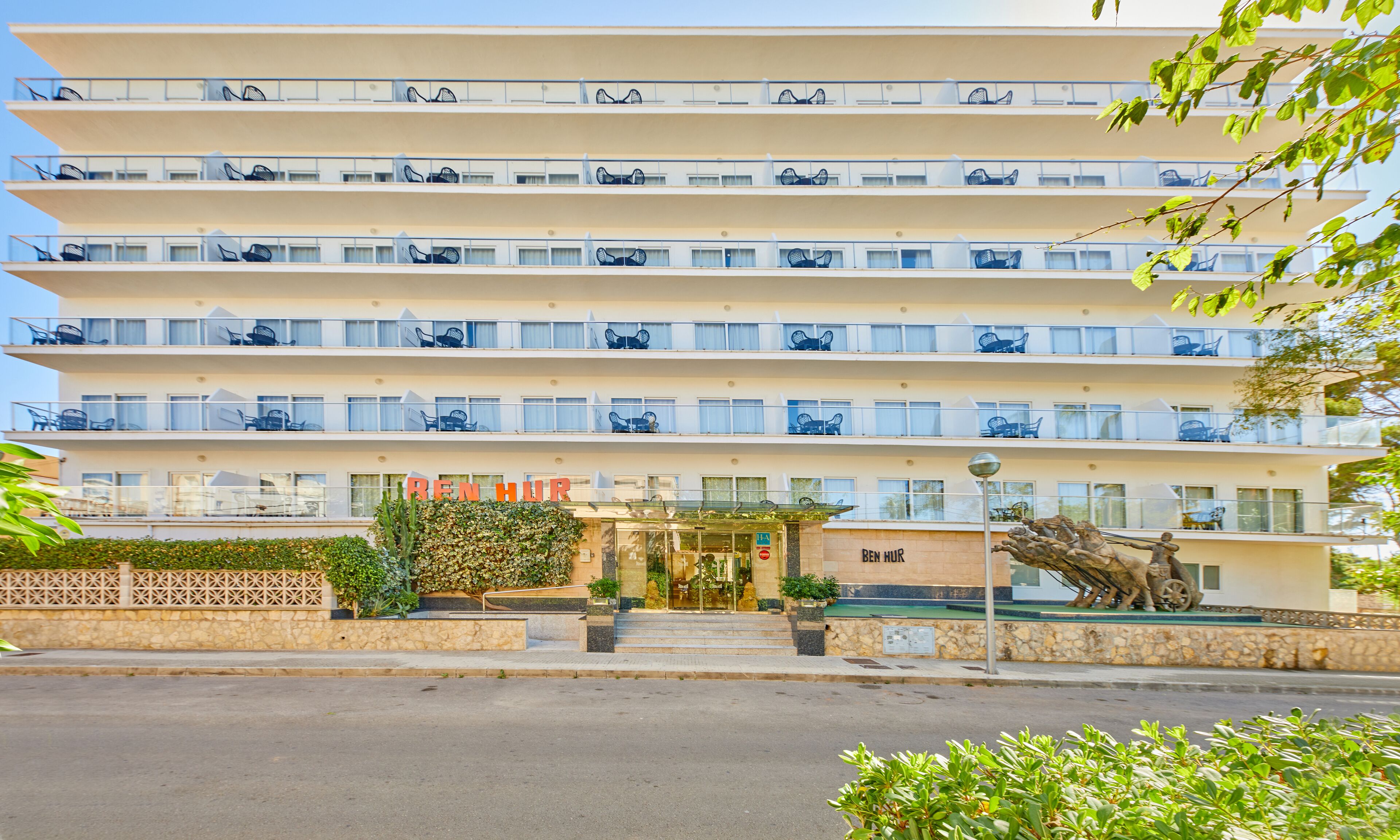 Un hotel de varios pisos con balcones, una entrada central y una estatua en el patio.