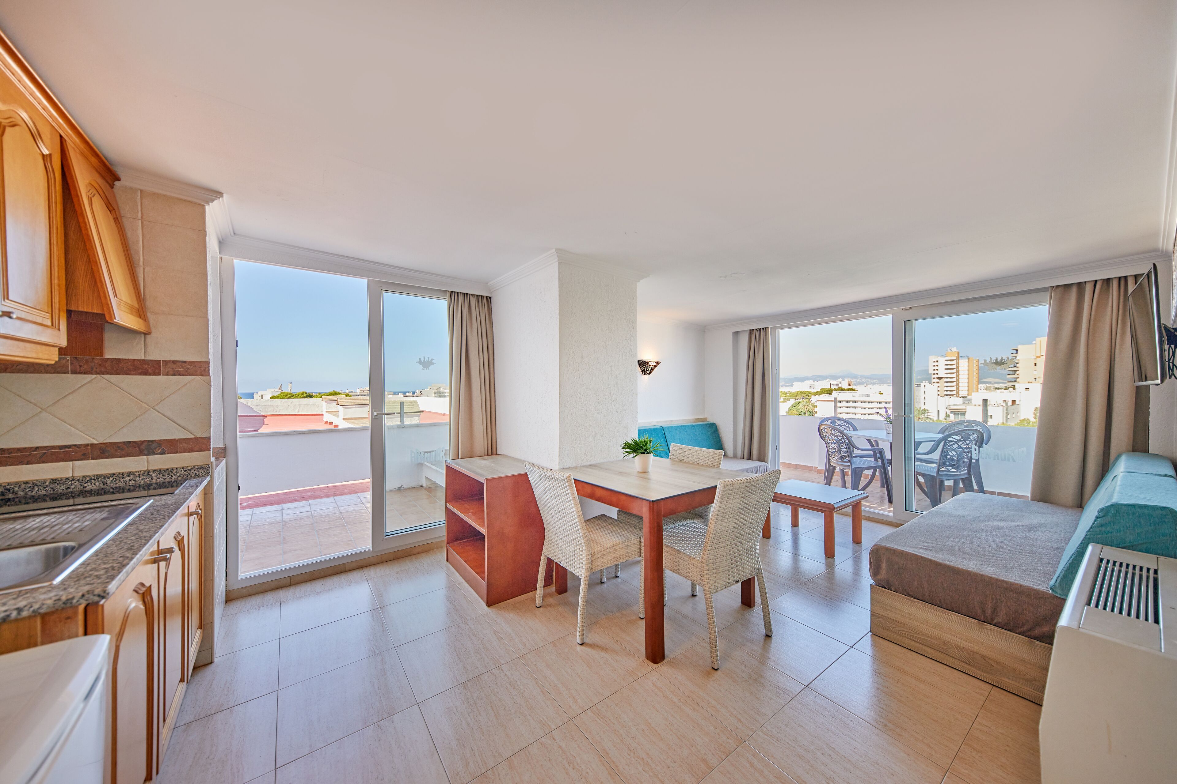 A modern kitchen with a dining area, a sofa, and a view of the city.