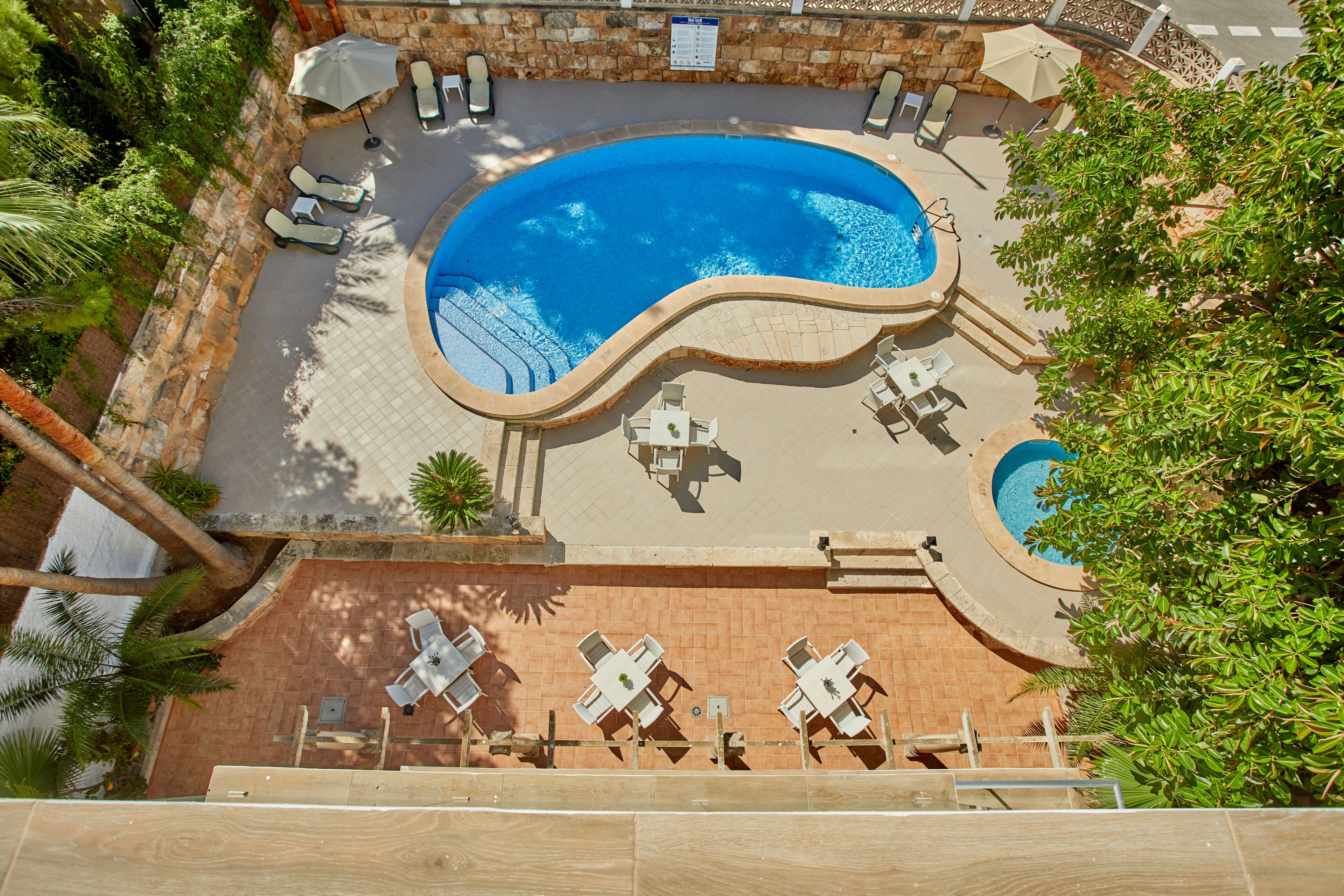 Uma piscina ao ar livre com espreguiçadeiras e mesas, cercada por um muro de pedra e vegetação.