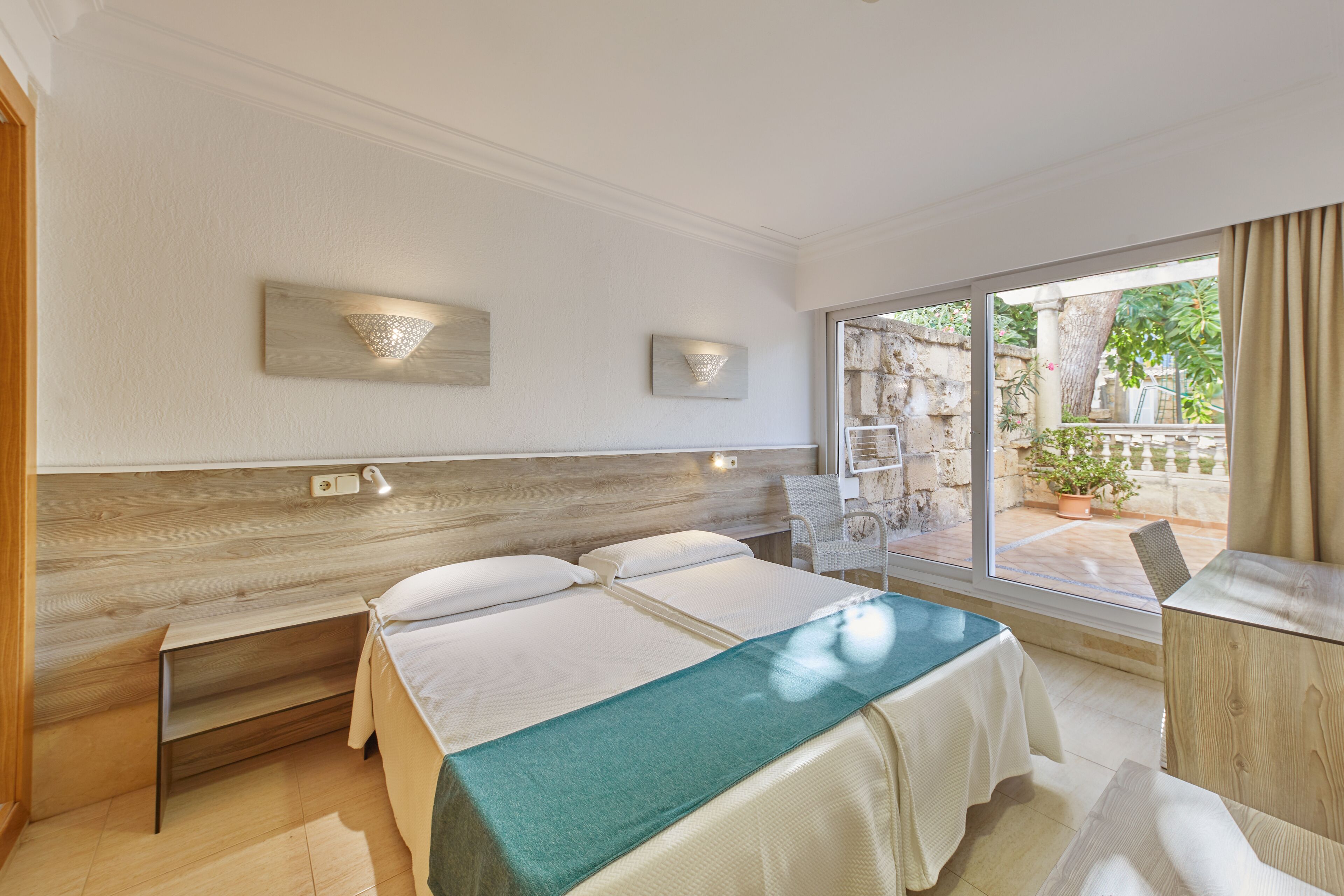 A hotel room with a large bed, a desk, and a view of the garden through the window.