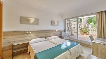 A hotel room with a large bed, a desk, and a view of the garden through the window.