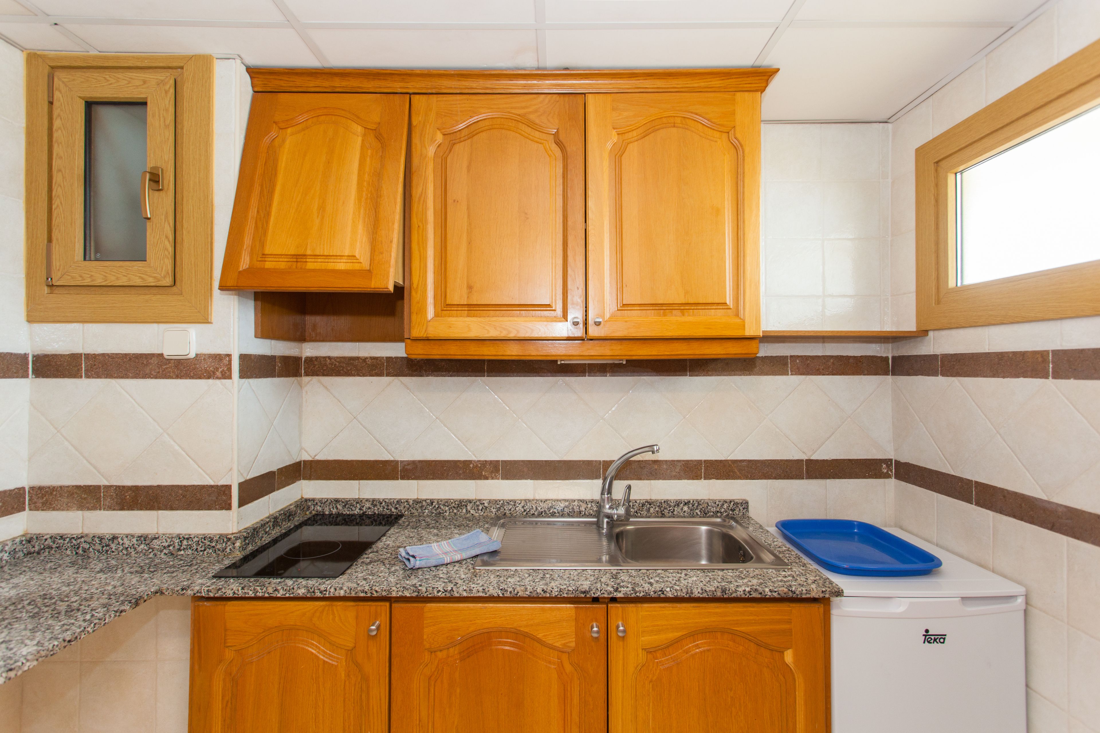 Une cuisine avec des meubles de rangement en bois, une cuisinière encastrée, un évier et une fenêtre.