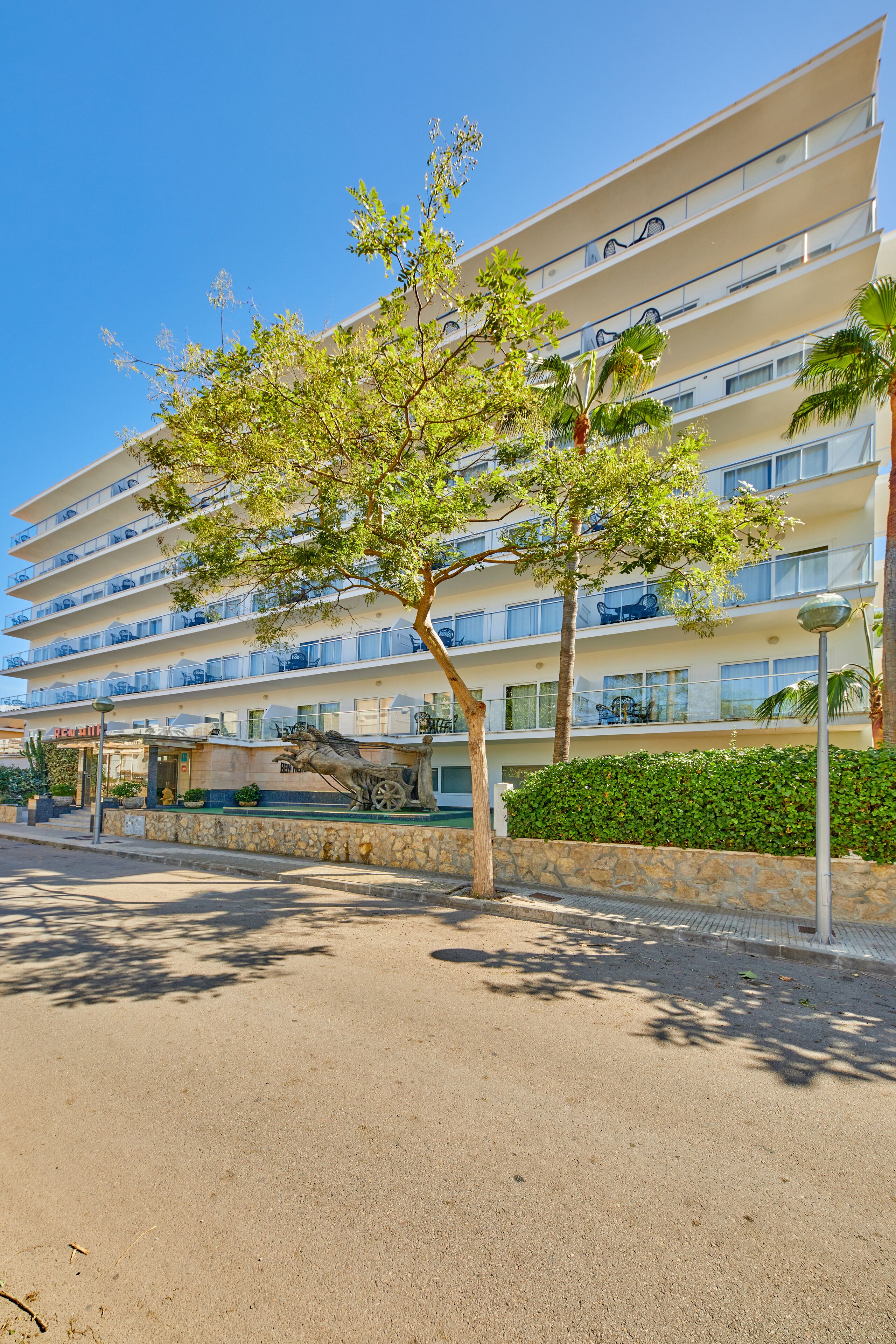 A multi-story hotel with balconies, a statue of a horse and carriage, and a clear blue sky.