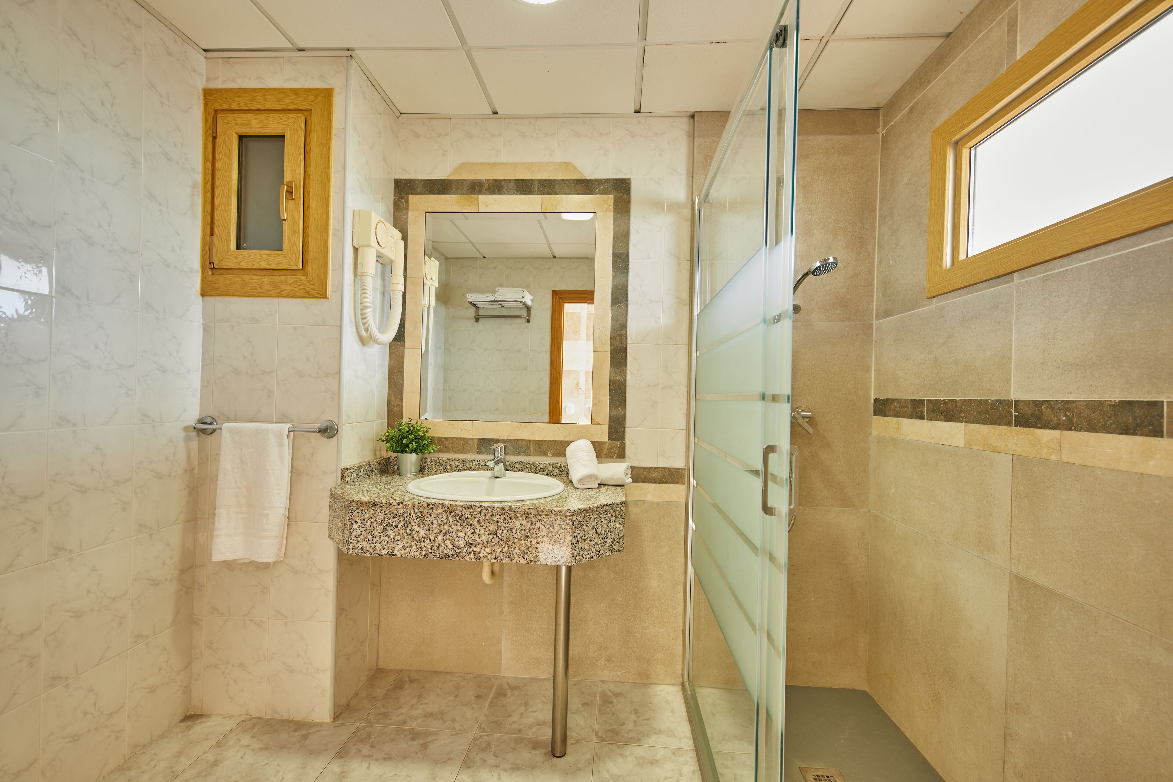 Een badkamer met een wastafel van graniet, een spiegel, een handdoekhouder en een douchehoek.