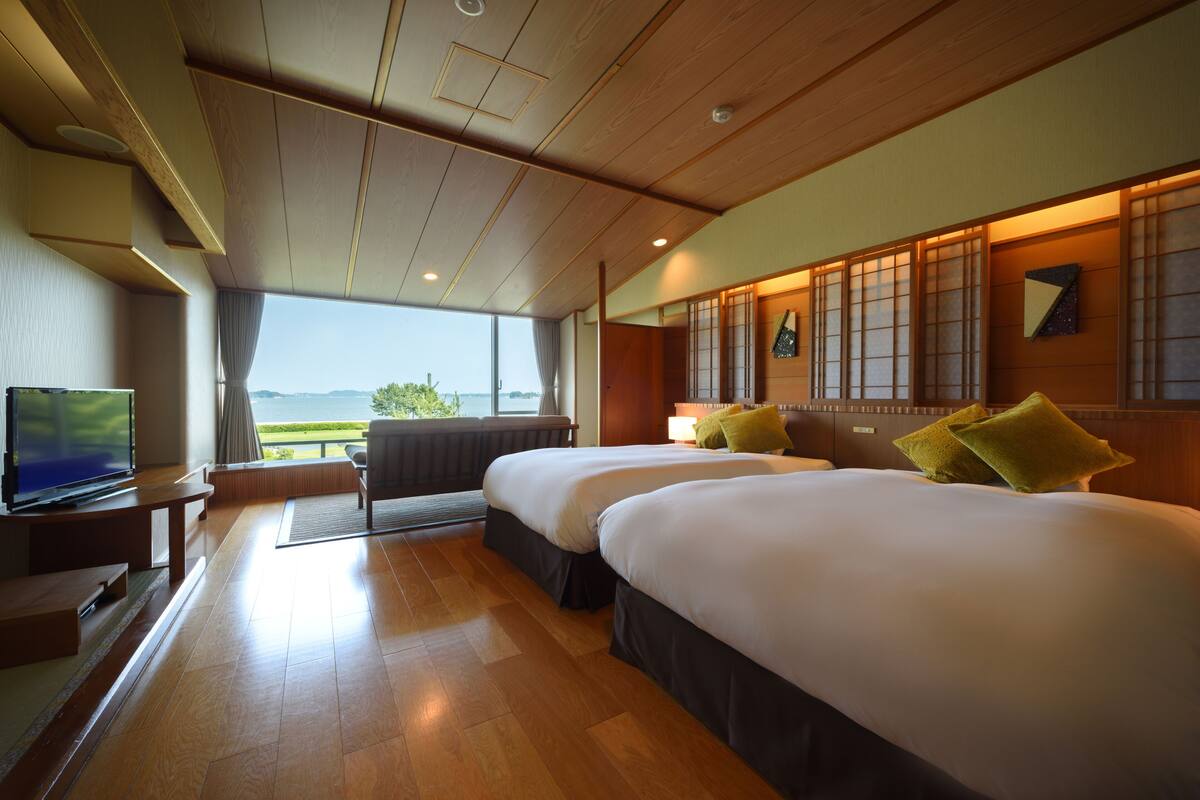 A hotel room with two beds, a TV, and a view of the sea.