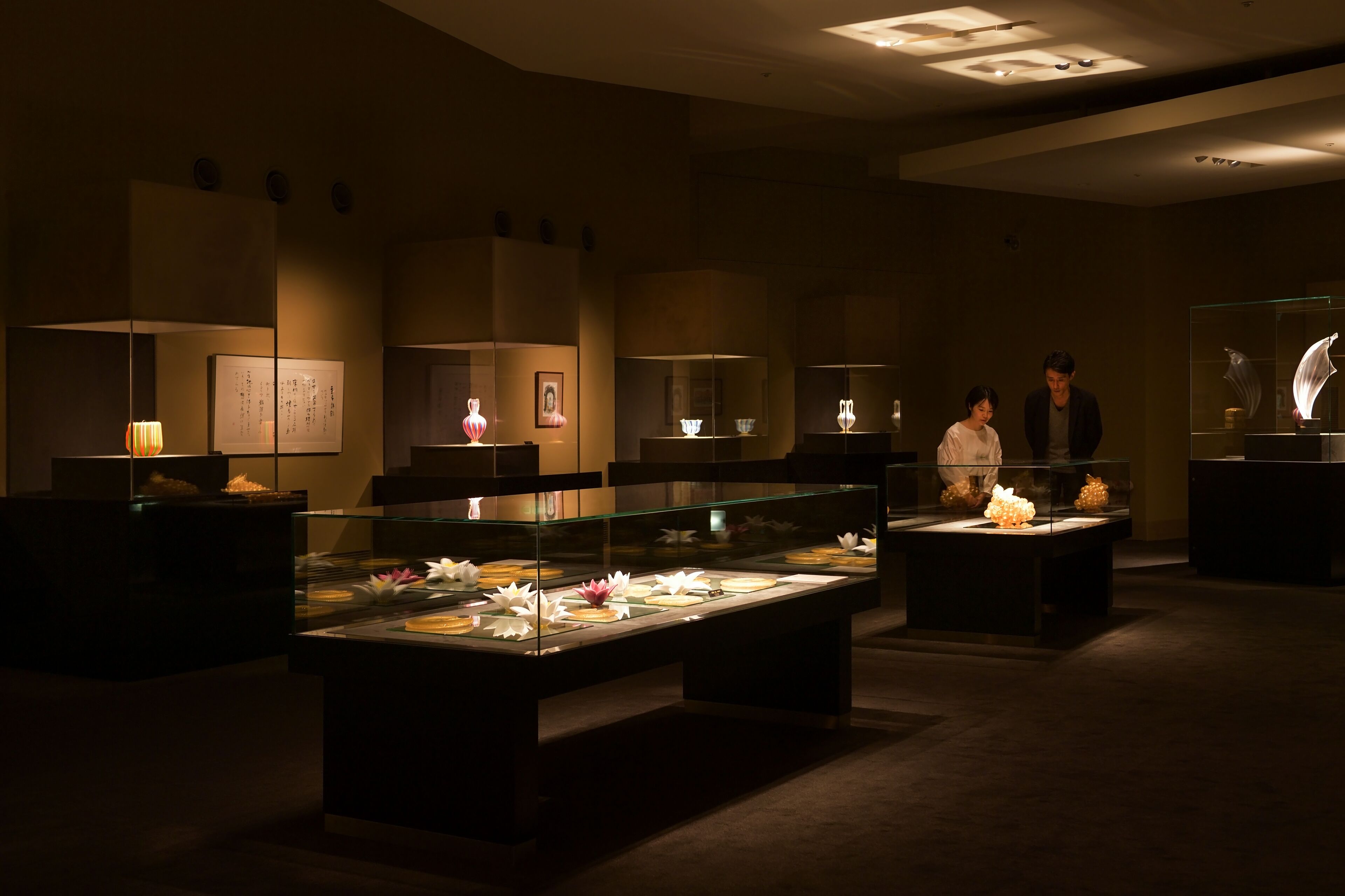Un museo o galería tenuemente iluminado con vitrinas de vidrio que exhiben diversos artefactos y esculturas.