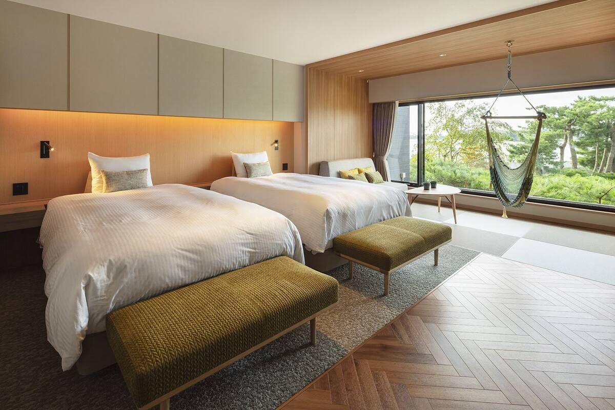 A modern hotel room with two beds, a bench, a small table, and a hammock.