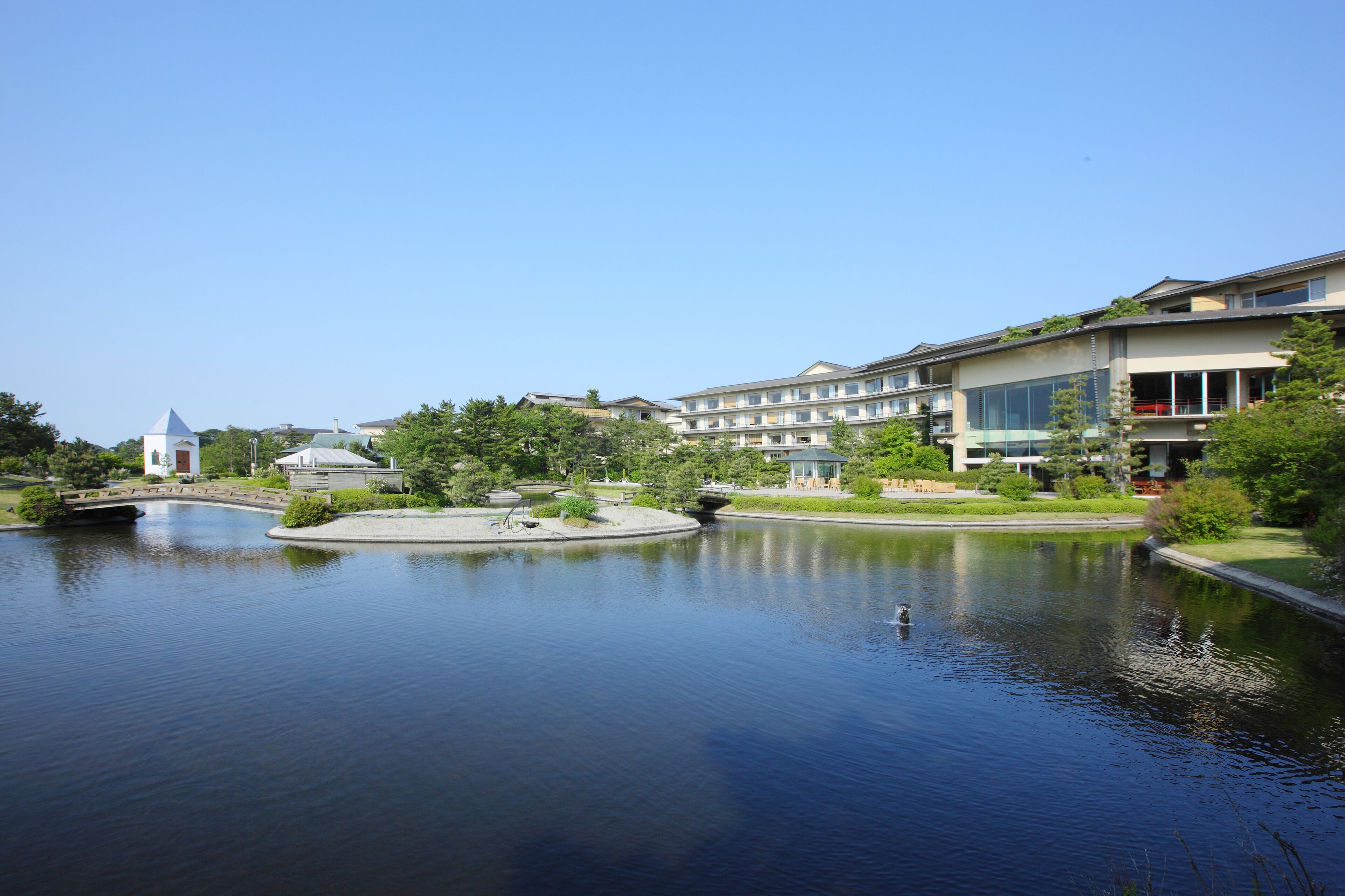 A calm lake with a bridge, surrounded by modern buildings with balconies and large windows.