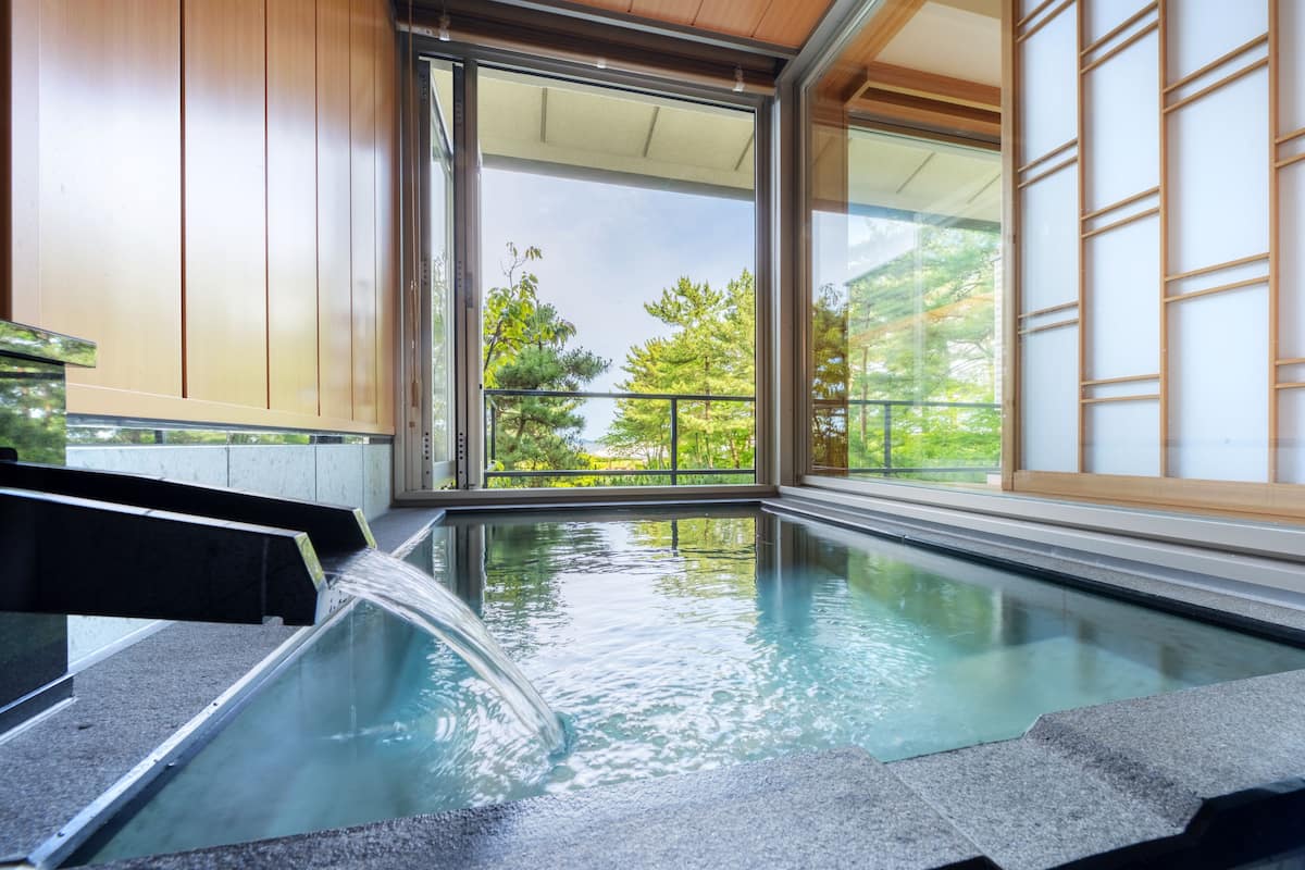 A modern indoor pool with a clear view of trees and a balcony.