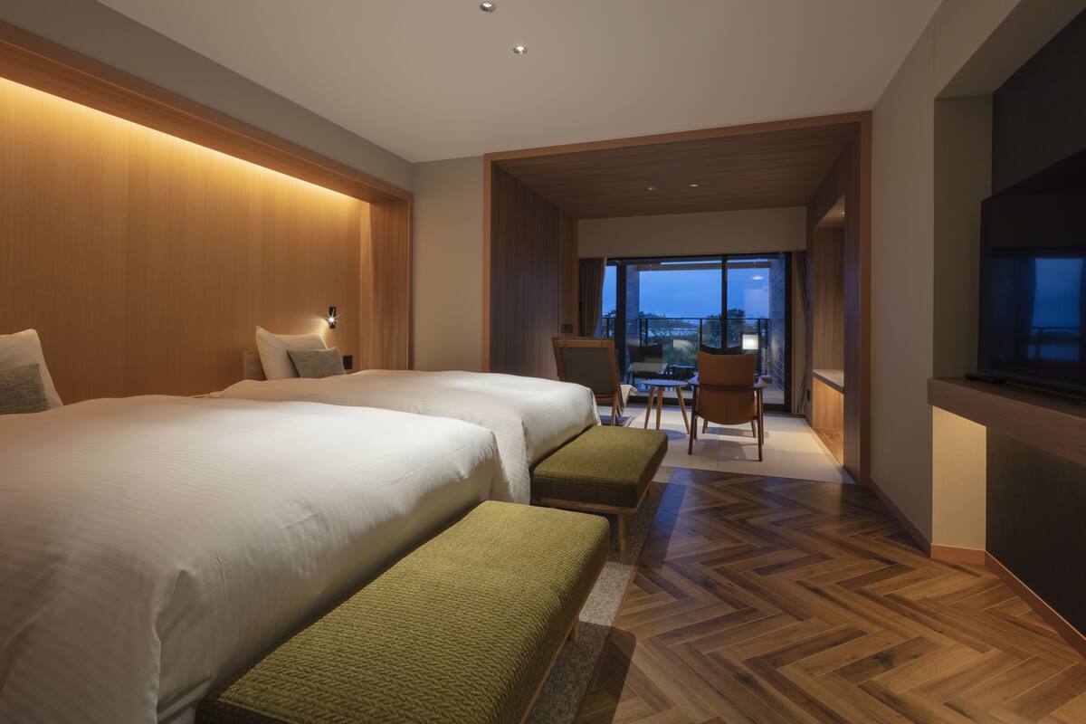 A modern hotel room with two large beds, a wooden floor, a balcony with a view, and a TV.