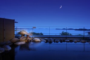 Un área de piscina tranquila al aire libre con rocas y una estructura de madera, con vistas a una masa de agua calma y terreno distante bajo un cielo crepuscular.
