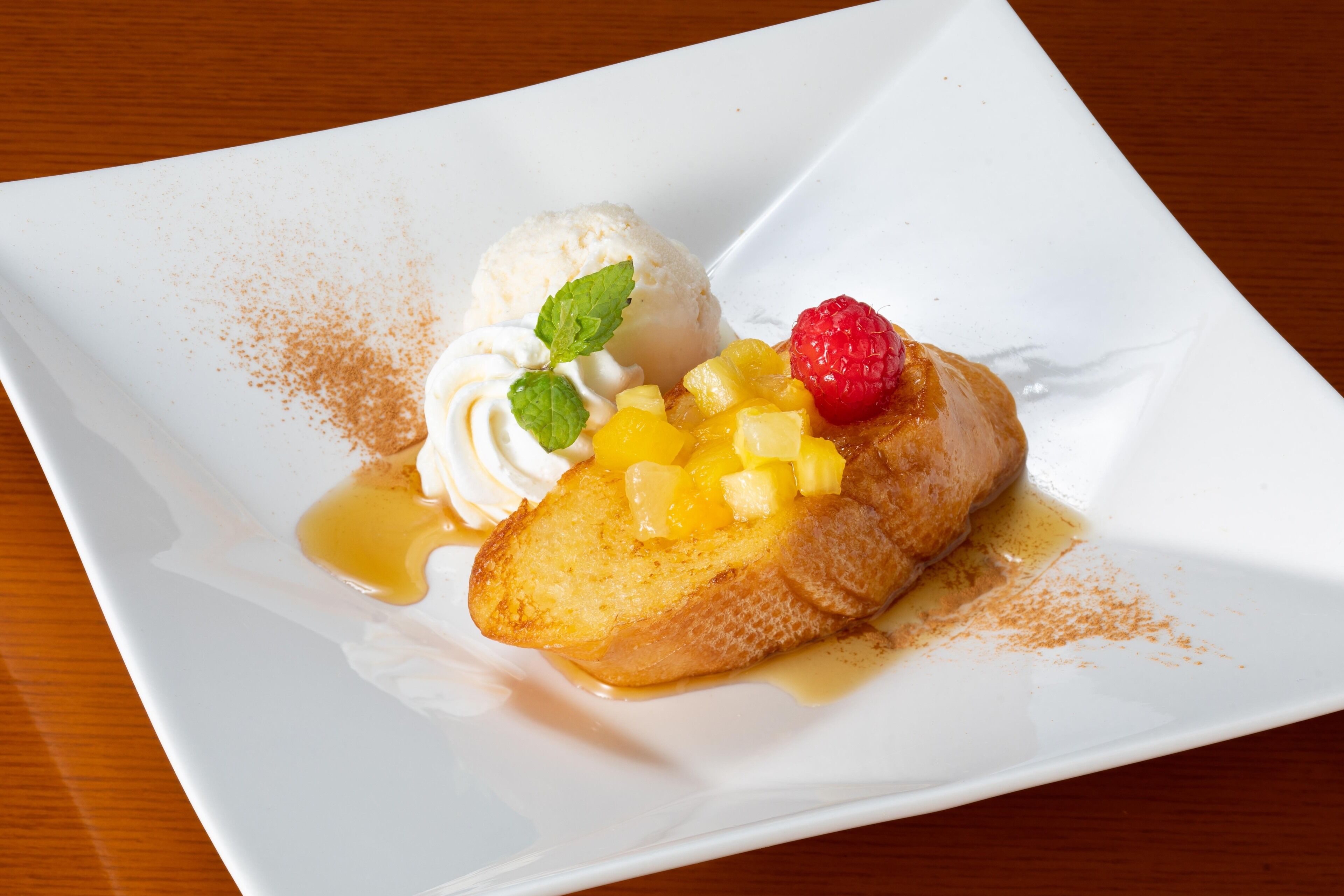 A dessert plate with a slice of pineapple upside-down cake, a scoop of vanilla ice cream, and a raspberry on a white plate.