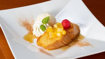 A dessert plate with a slice of pineapple upside-down cake, a scoop of vanilla ice cream, and a raspberry on a white plate.