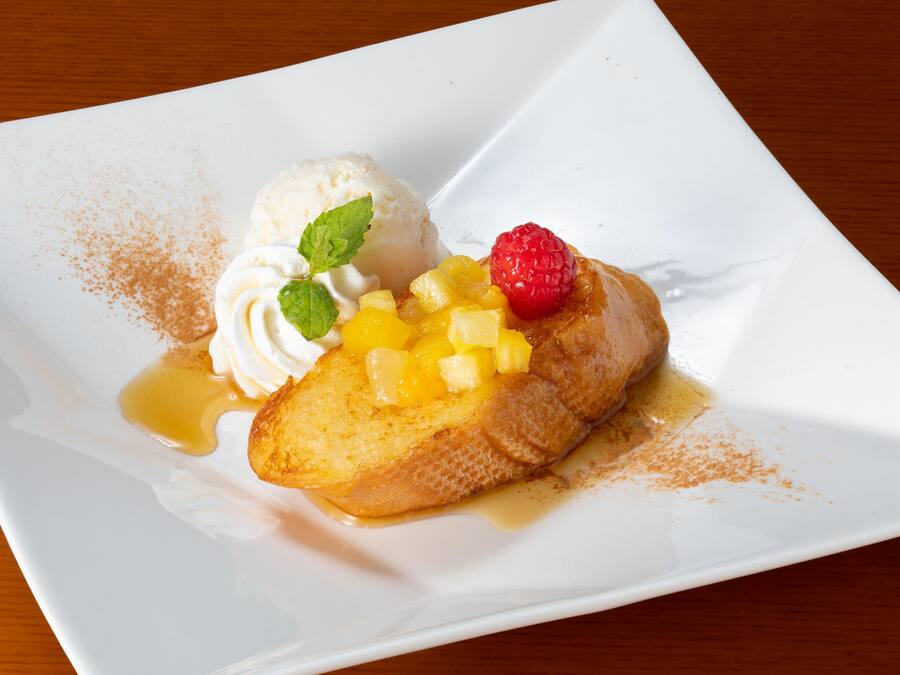 A dessert plate with a slice of pineapple upside-down cake, a scoop of vanilla ice cream, and a raspberry on a white plate.
