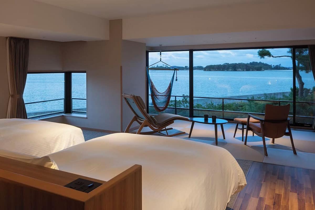 A hotel room with two beds, a hammock, a table, and a view of a lake.