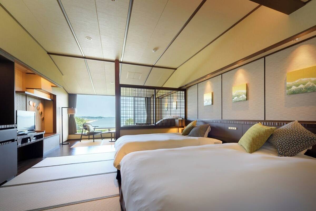 A hotel room with two beds, a desk with a TV, and a view of the sea.