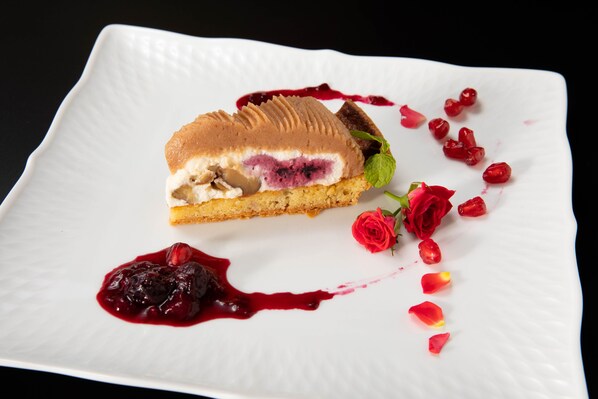 Un dessert servi dans une assiette blanche de forme carrée, décoré de baies rouges et d’une rose.